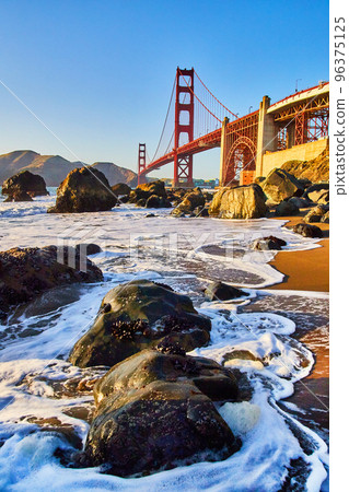 Waves crash around rocks on beach next to Golden Gate Bridge in San Francisco near sunset Waves crash around rocks on beach next to Golden Gate Bridge in San Francisco near sunset 96375125
