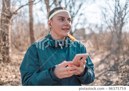 Social media and sport. Smiling athletic young woman in fashion sportswear looking at smartphone at autumn park 96375759