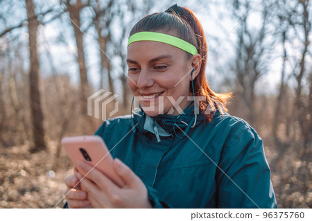 Social media and sport. Smiling athletic young woman in fashion sportswear looking at smartphone at autumn park 96375760