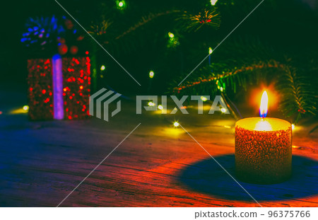 a red Christmas box with a gift and a  burning candle on the background of a natural fir tree with Christmas lights 96375766