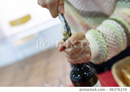 Corkscrew. Came. Time to open the bottle of red wine with the corkscrew. Woman's hands holding the bottle while opening the cork. Horizontal photography. 96376239