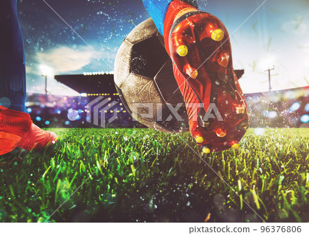 Football scene at night match with close up of a soccer shoe hitting the ball with power 96376806