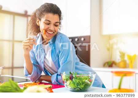 Young woman in the home kitchen eating a genuine salad with fresh vegetables Young woman in the home kitchen eating a genuine salad with fresh vegetables 96377899
