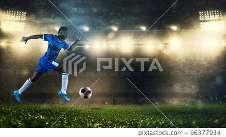 Soccer player in blue uniform sprinting fast with the ball at the stadium Soccer player in blue uniform sprinting fast with the ball at the stadium 96377934