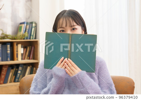 Young woman covering her eyes with a book Young woman covering her eyes with a book 96379410