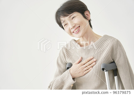 Middle-aged woman using crutches with a smile White background 96379875