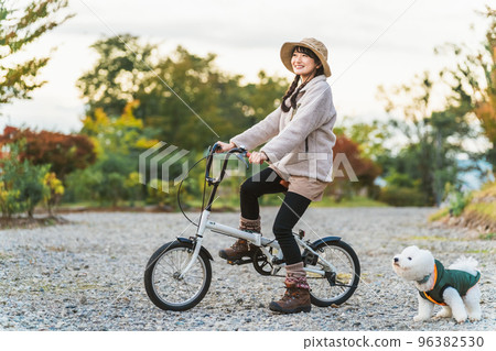 Asian woman cycling on a bicycle at a campsite in autumn and winter with her dog Asian woman cycling on a bicycle at a campsite in autumn and winter with her dog 96382530
