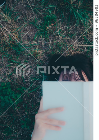 Photo of a young woman lying down and reading a book Photo of a young woman lying down and reading a book 96384983