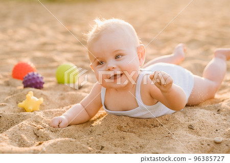 A happy little boy is lying on a sandy beach near the sea in the rays of the setting sun A happy little boy is lying on a sandy beach near the sea in the rays of the setting sun 96385727