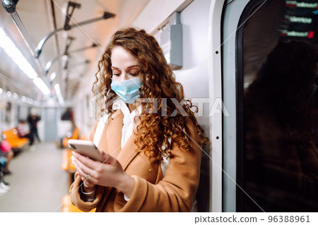 Girl in protective sterile medical mask on her face with a phone in a subway car. Covid-19 Girl in protective sterile medical mask on her face with a phone in a subway car. Covid-19 96388961
