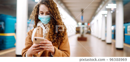 Girl in protective sterile medical mask with a phone at subway station. Woman, wear face mask. 96388969