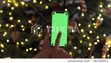 Closeup woman hand is holding chroma key green screen touching on christmas background. Using phone with green mock-up, surfing internet. Closeup woman hand is holding chroma key green screen touching on christmas background. Using phone with green mock-up, surfing internet. 96389051