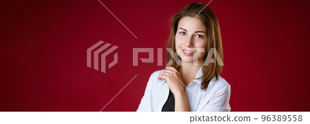 A woman is standing and smiling against a red studio background 96389558