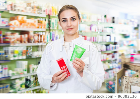 Young female is welcoming and holding medicines in hall of apothecary. Young female is welcoming and holding medicines in hall of apothecary. 96392136