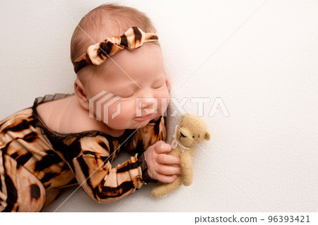 Sleeping newborn girl in the first days of life on a white background. Macro studio portrait of a child. Image of a tiger cub. Newborn baby in tiger pajamas. Striped black and orange baby clothes. Sleeping newborn girl in the first days of life on a white background. Macro studio portrait of a child. Image of a tiger cub. Newborn baby in tiger pajamas. Striped black and orange baby clothes. 96393421