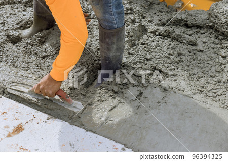 An employee is holding steel trowel as he smooths leveling over freshly poured concrete sidewalk in construction zone An employee is holding steel trowel as he smooths leveling over freshly poured concrete sidewalk in construction zone 96394325