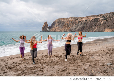 A group of five female friends are doing exercises on the beach. Beach holiday concept, healthy lifestyle A group of five female friends are doing exercises on the beach. Beach holiday concept, healthy lifestyle 96394920