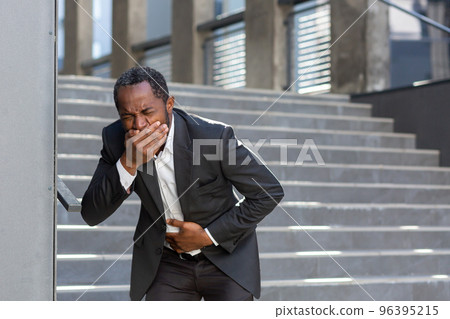 Nausea and pain in the stomach, a businessman from outside the office building is sick, a man is holding his hand on his stomach in a business suit, he got sick with poor-quality food. 96395215