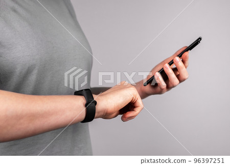 Woman with fitness bracelet at wrist using mobile app at phone for checking physical activity results or connecting watches to smartphone. Healthy lifestyle concept 96397251