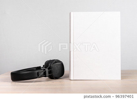 Audiobook concept. Headphones and book mockup with white blank cover at wooden table. Novel listening or reading. Literature advertising Audiobook concept. Headphones and book mockup with white blank cover at wooden table. Novel listening or reading. Literature advertising 96397401