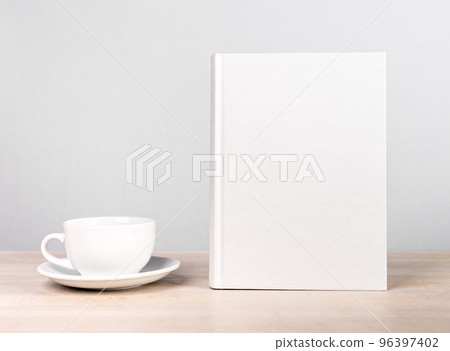 Book mockup and cup at wooden table. Reading leisure, relaxation with tea or coffee mug, harmony concept. Novel, encyclopedia, code template with empty cover. 96397402