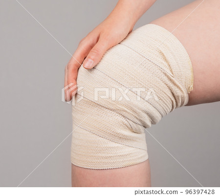 Woman wrapping compression bandage around painful knee to relieve pain or prevent injury. Muscle sprains, strains, overuse treatment. Health problems, medical conditions. Woman wrapping compression bandage around painful knee to relieve pain or prevent injury. Muscle sprains, strains, overuse treatment. Health problems, medical conditions. 96397428