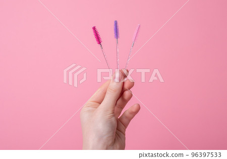 Hand with eyelash wands, brushes for separating lashes after applying mascara, grooming extensions on pink background. Beauty, makeup, face care concept. Hand with eyelash wands, brushes for separating lashes after applying mascara, grooming extensions on pink background. Beauty, makeup, face care concept. 96397533