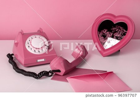 Retro phone with heart mirror and envelopes at table. Still life in pink color. Valentines day concept Retro phone with heart mirror and envelopes at table. Still life in pink color. Valentines day concept 96397707