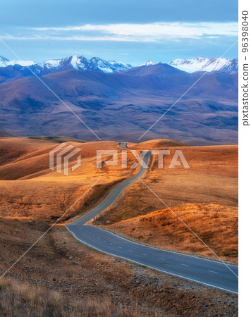 Vertical view of a picturesque road stretching into the distance through the picturesque autumn hills. Winding asphalted clean road stretches into the distance to the snow-capped mountains. Vertical view of a picturesque road stretching into the distance through the picturesque autumn hills. Winding asphalted clean road stretches into the distance to the snow-capped mountains. 96398040