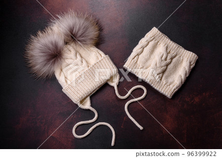 Beautiful white knitted winter cap with pompons on a dark concrete background Beautiful white knitted winter cap with pompons on a dark concrete background 96399922
