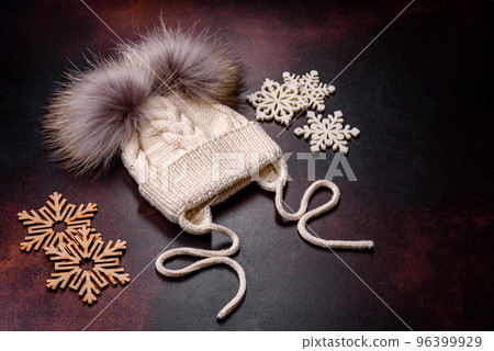 Beautiful white knitted winter cap with pompons on a dark concrete background 96399929