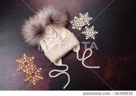 Beautiful white knitted winter cap with pompons on a dark concrete background 96399930