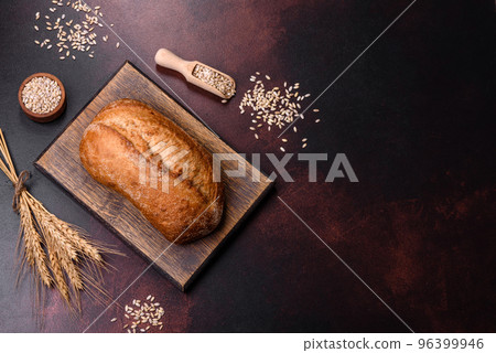 A loaf of brown bread with grains of cereals on a wooden cutting board 96399946