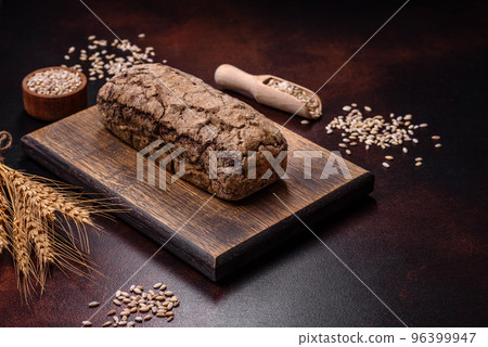 A loaf of brown bread with grains of cereals on a wooden cutting board 96399947