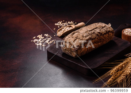 A loaf of brown bread with grains of cereals on a wooden cutting board 96399959