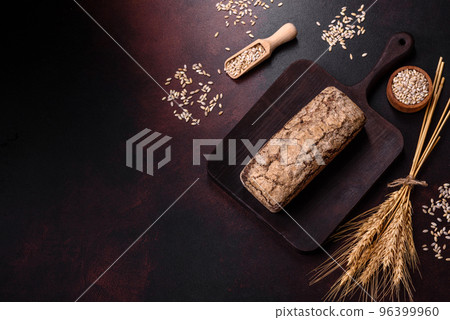 A loaf of brown bread with grains of cereals on a wooden cutting board 96399960