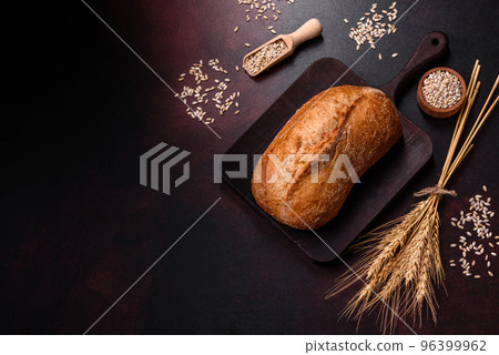A loaf of brown bread with grains of cereals on a wooden cutting board 96399962