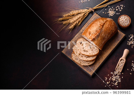 A loaf of brown bread with grains of cereals on a wooden cutting board 96399981