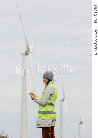 female engineer in a protective vest takes measurements of the speed of wind turbines. electricity is generated by wind 96402064