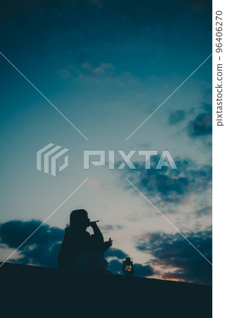 Silhouette photo of a young woman sitting and blowing bubbles 96406270