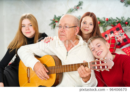 Grandfather playing guitar during christmas for grandchildren. Happy man 60s playing guitar christmas songs. 96406670