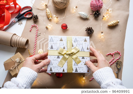 Pack a gift for Christmas and new year in kraft paper, cones, tape, scissors. Tags with mock up, natural decor, hand made, DIY. Festive mood. Flatlay, background 96409991