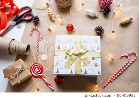 Pack a gift for Christmas and new year in kraft paper, cones, tape, scissors. Tags with mock up, natural decor, hand made, DIY. Festive mood. Flatlay, background 96409992
