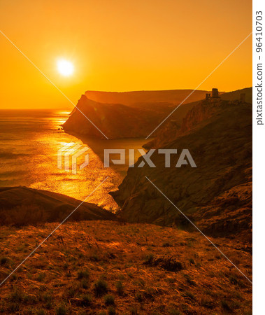 A red burning sunset with the silhouett of a cliff and castle over the sea A red burning sunset with the silhouett of a cliff and castle over the sea 96410703