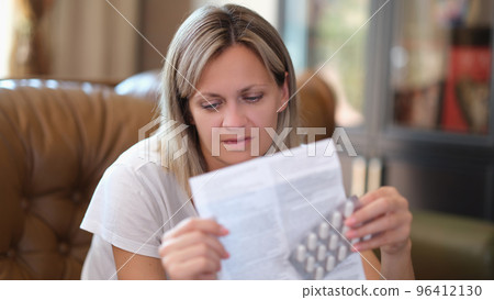 Woman with package of medical pills reads leaflet with instructions for taking pills. Woman with package of medical pills reads leaflet with instructions for taking pills. 96412130