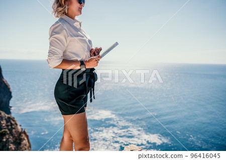 Digital nomad, Business woman working on tablet pc pad computer by the sea. Pretty lady with tablet pc on the sea, makes a business transaction online from distance. Freelance, remote work on vacation 96416045