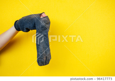old smelly holey sock in hand on a yellow background old smelly holey sock in hand on a yellow background 96417773