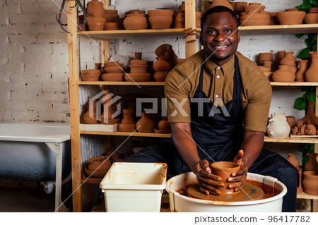 happy dark-skinned african american businessman potter man molding In workshop. sculptor pottering clay pot in a studio workplace. creativity and inspiration of the artist 96417782
