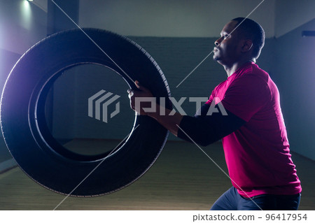 muscular shirtless young african american man in sportswear tire exercising with tyre in gym on a black background in the studio workshop muscular shirtless young african american man in sportswear tire exercising with tyre in gym on a black background in the studio workshop 96417954
