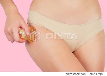 Anti-cellulite massage.Woman in beige panties massaging thigh massage receiving a professional anti cellulite cans (jars, banks) ventuza vacuum leg hips and butt ass on a pink background in the studio Anti-cellulite massage.Woman in beige panties massaging thigh massage receiving a professional anti cellulite cans (jars, banks) ventuza vacuum leg hips and butt ass on a pink background in the studio 96417989
